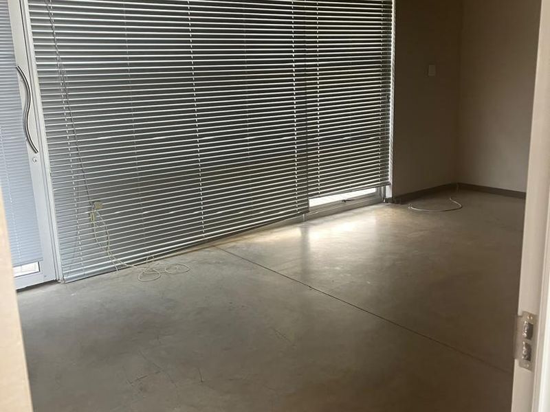 An empty office space featuring polished concrete floors, large sliding glass doors with venetian blinds, and functional overhead lighting.