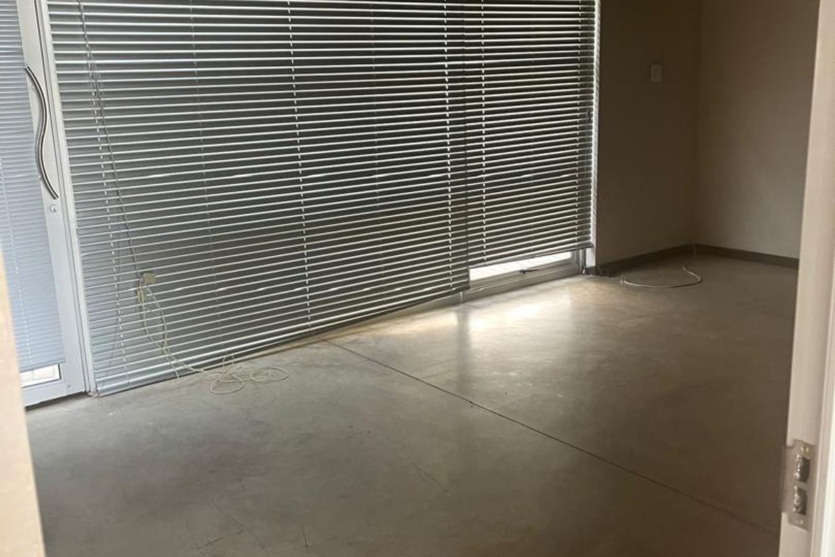An empty office space featuring polished concrete floors, large sliding glass doors with venetian blinds, and functional overhead lighting.