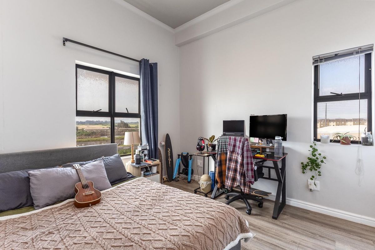 A well-lit bedroom featuring laminate flooring, coved ceilings, and large aluminium-framed windows offering natural light and exterior views.