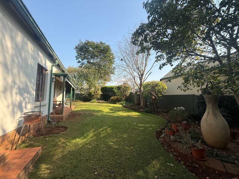 A well-maintained rear garden featuring a lush lawn, established trees, a boundary wall, and a covered patio area.