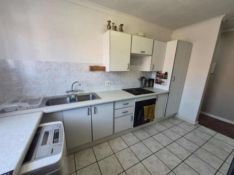 Functional kitchen featuring laminate countertops, built-in cabinetry, integrated oven and hob, and tiled flooring with a neutral splashback.