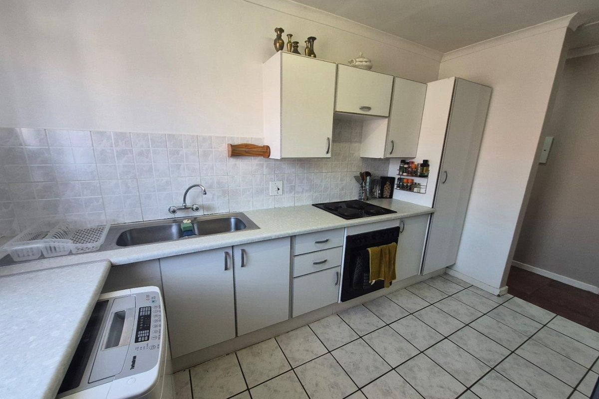 Functional kitchen featuring laminate countertops, built-in cabinetry, integrated oven and hob, and tiled flooring with a neutral splashback.