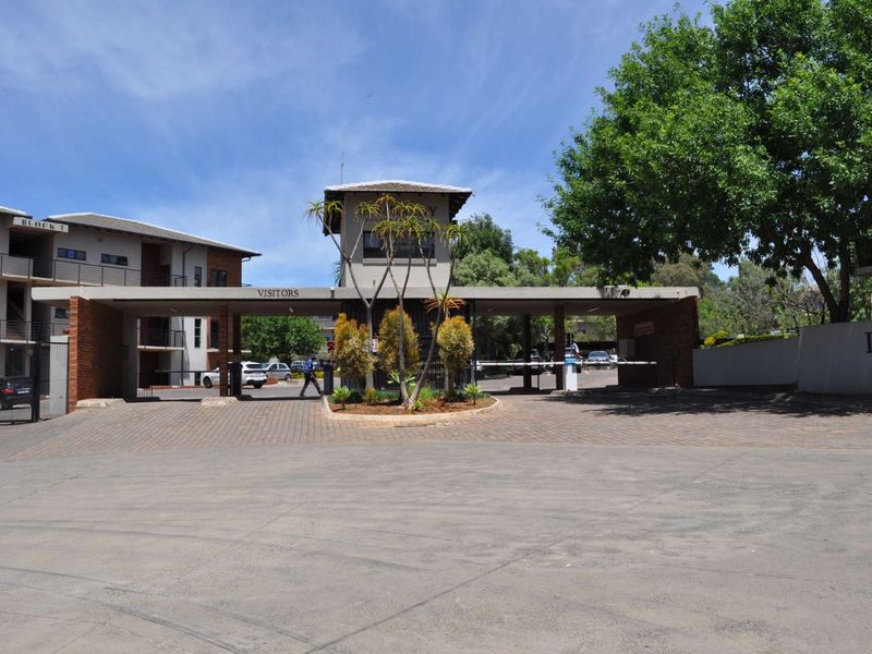 The main entrance to the office park featuring a security gatehouse, boom gate access control, and a paved driveway.