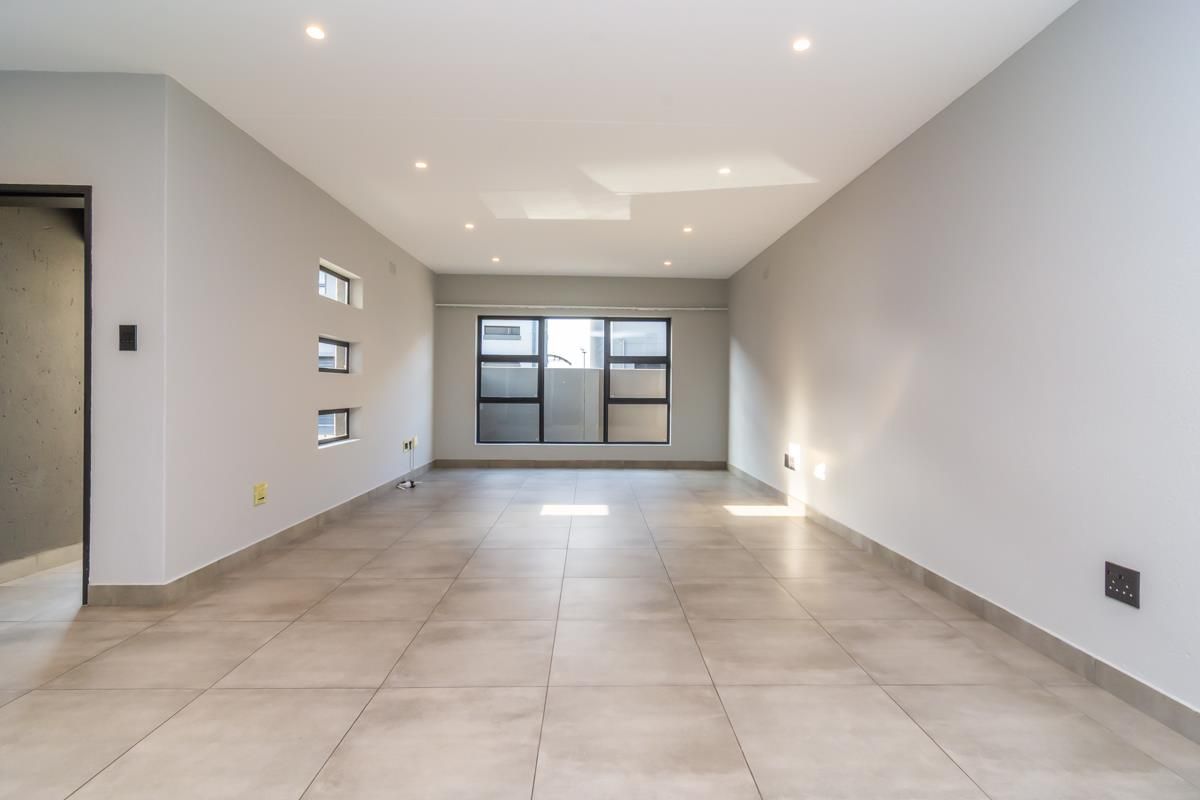 A bright, spacious, and empty living area featuring neutral tiled flooring, recessed ceiling lighting, and modern aluminium-framed windows.