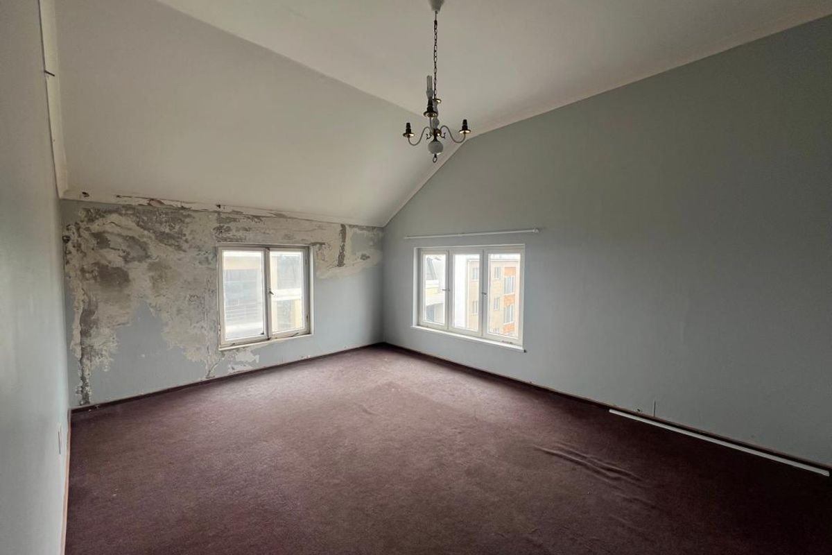 An empty bedroom featuring vaulted ceilings, large windows, and significant wall surface damage requiring repair and redecoration.