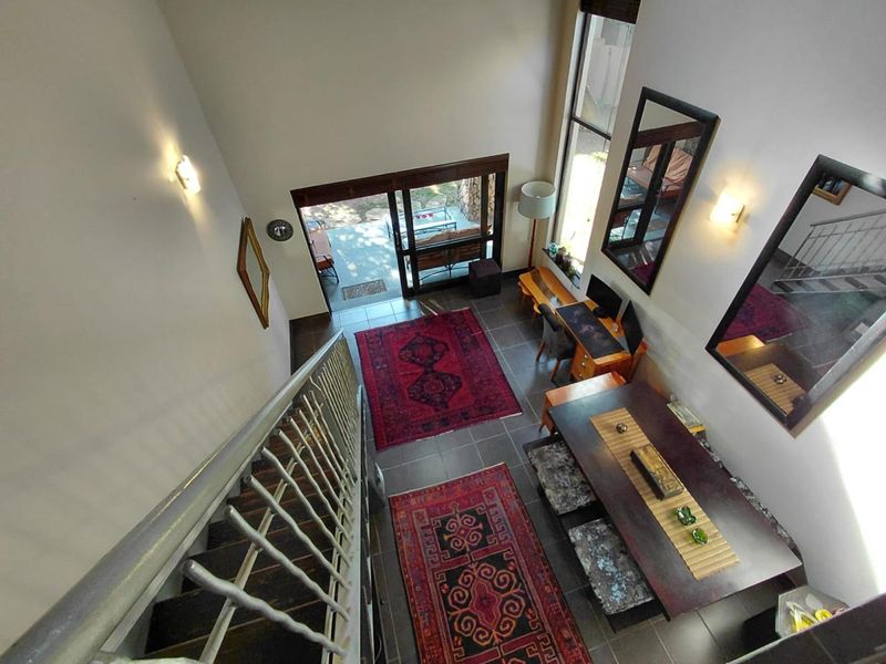 A high-ceiling living area featuring tiled floors, a staircase with a metal balustrade, and sliding glass doors leading to an outdoor patio.