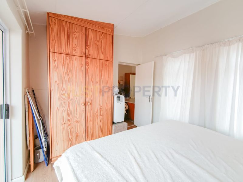 A bedroom featuring a large built-in wooden wardrobe, neutral walls, and access to an adjoining space through a doorway.