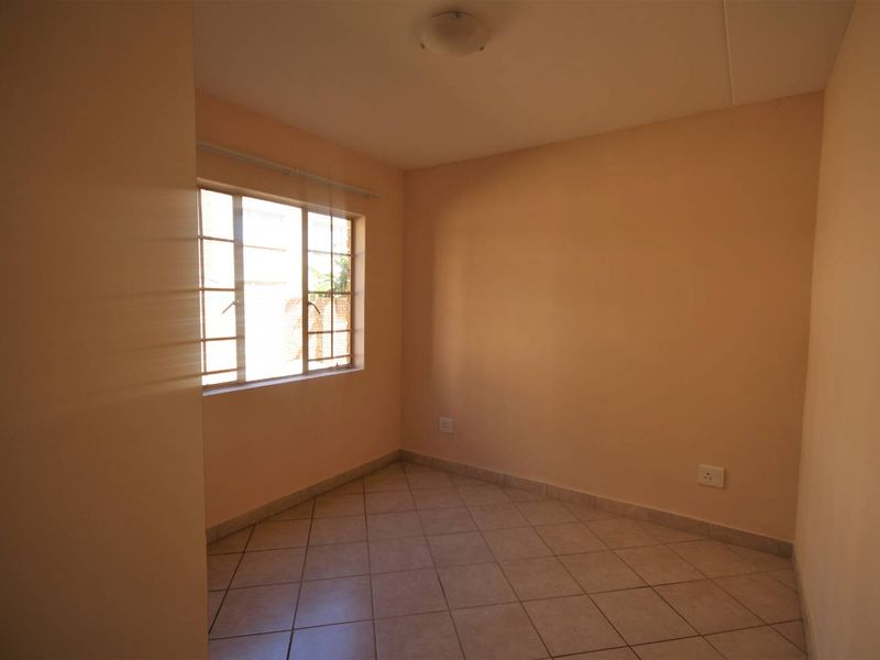 An empty bedroom featuring tiled flooring, neutral wall paint, and a steel-framed window providing natural light.