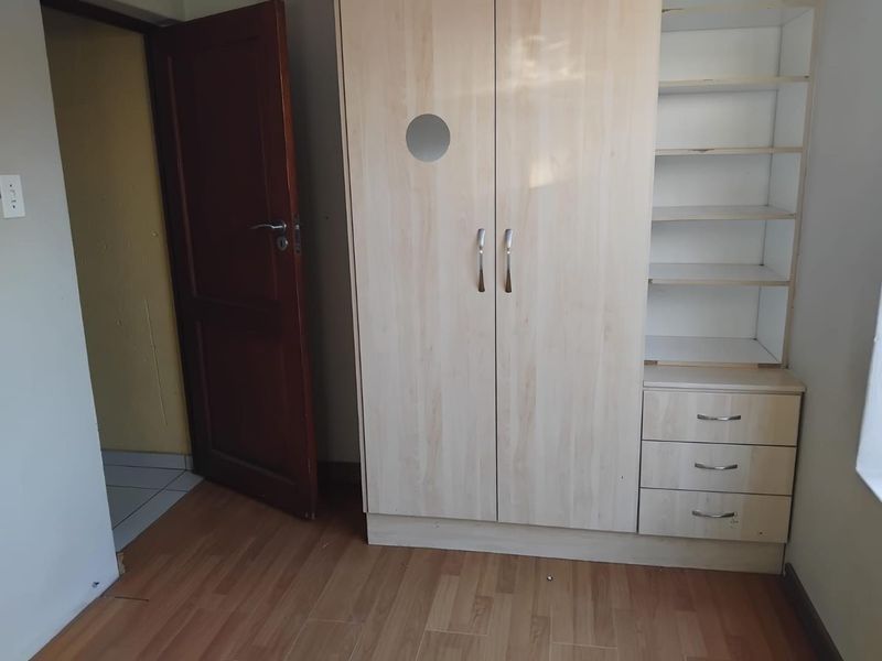 A bedroom featuring light wood-finish built-in cabinetry with integrated shelving and drawers, complemented by laminate flooring.