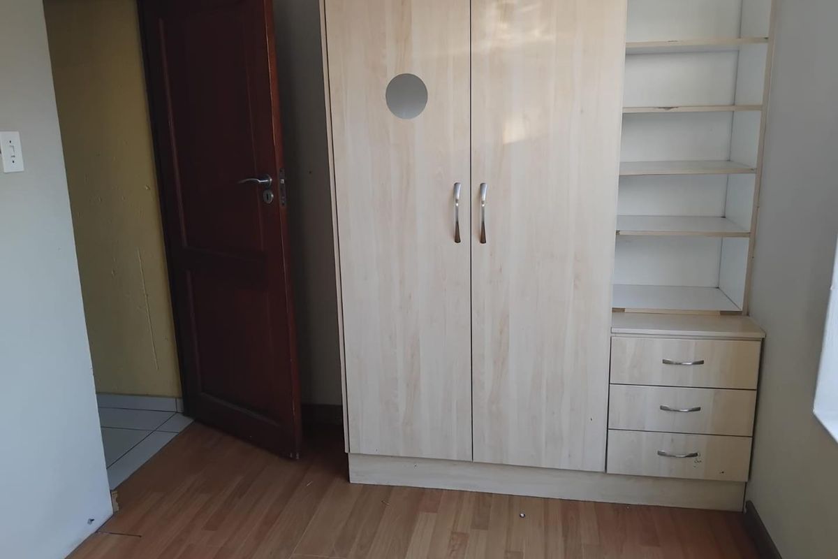 A bedroom featuring light wood-finish built-in cabinetry with integrated shelving and drawers, complemented by laminate flooring.