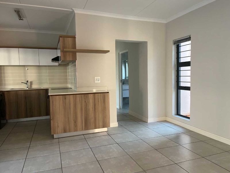 An open-plan kitchen and living area featuring modern wood-finish cabinetry, tiled flooring, and a view through to the bathroom.
