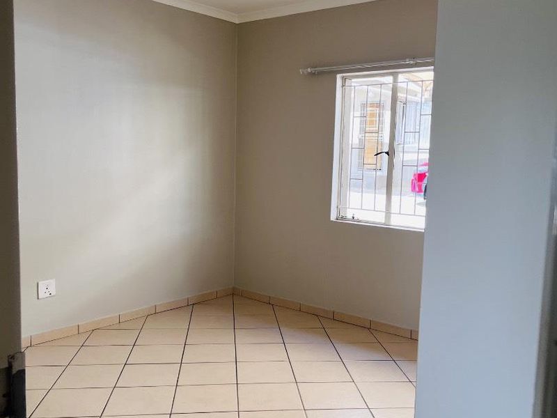 An empty bedroom featuring neutral wall paint, tiled flooring, and a window fitted with security bars.