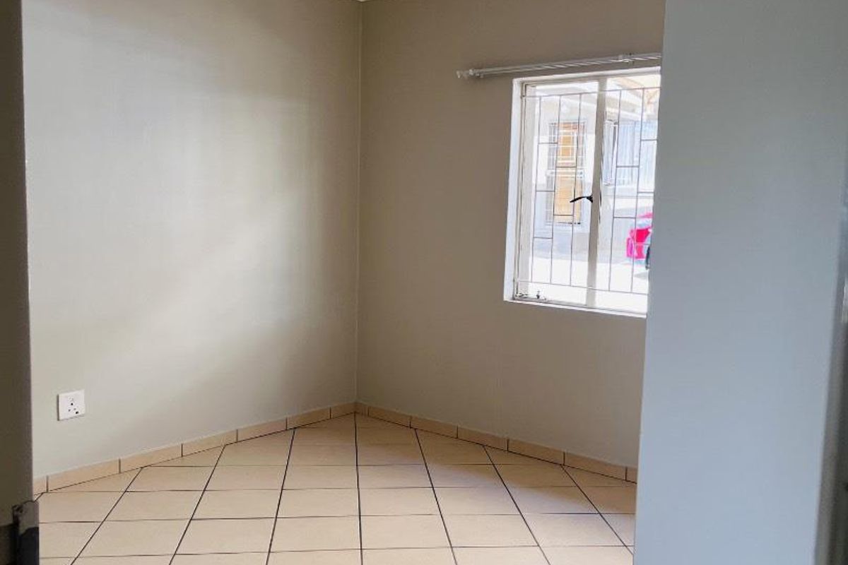 An empty bedroom featuring neutral wall paint, tiled flooring, and a window fitted with security bars.