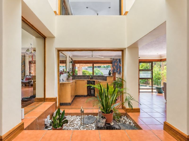Spacious open-plan living area featuring a central indoor water feature, tiled flooring, and a view through to the kitchen and garden.