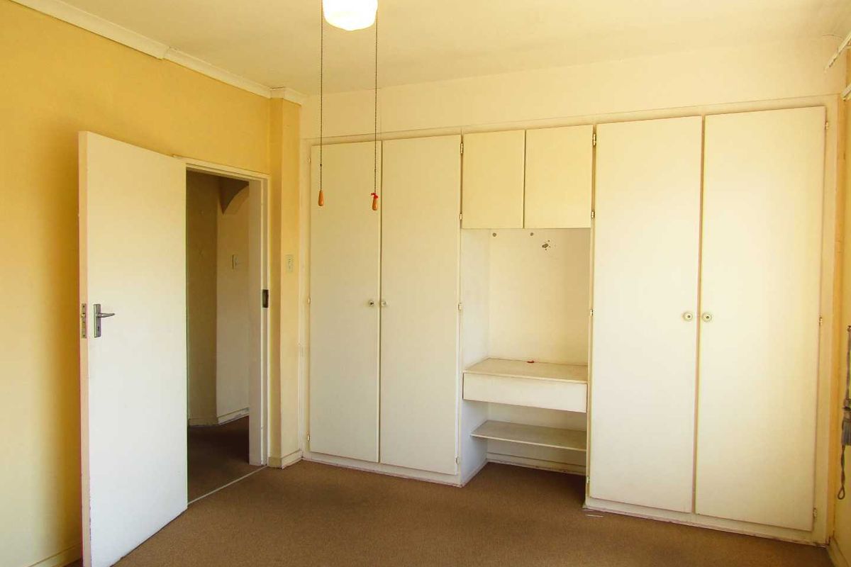 A vacant bedroom featuring built-in cupboards with an integrated vanity, carpeted flooring, and neutral wall finishes, offering a blank canvas for renovation.