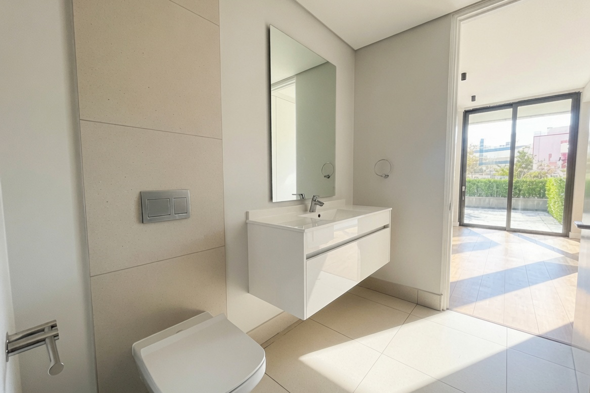 Modern bathroom featuring a wall-mounted toilet, floating vanity with integrated basin, and large mirror, leading to an outdoor patio area.