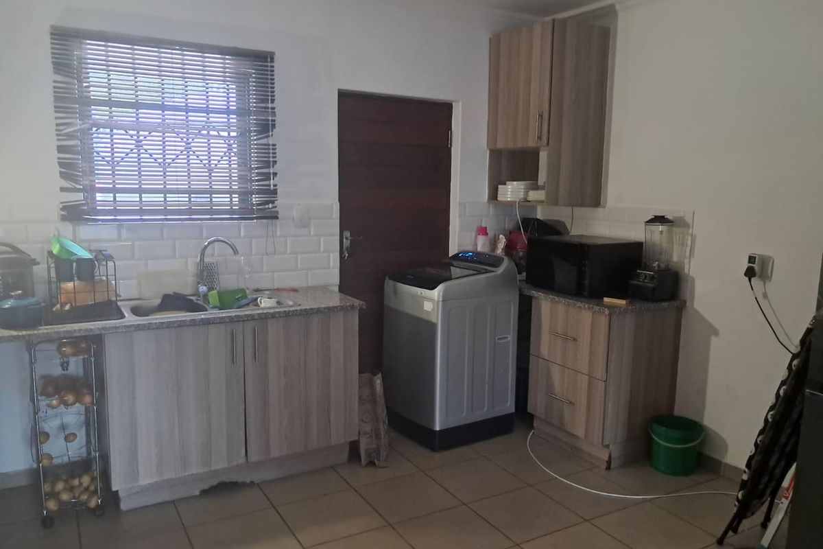 Functional kitchen featuring wood-look cabinetry, subway tile backsplash, stainless steel sink, and dedicated space for laundry appliances.