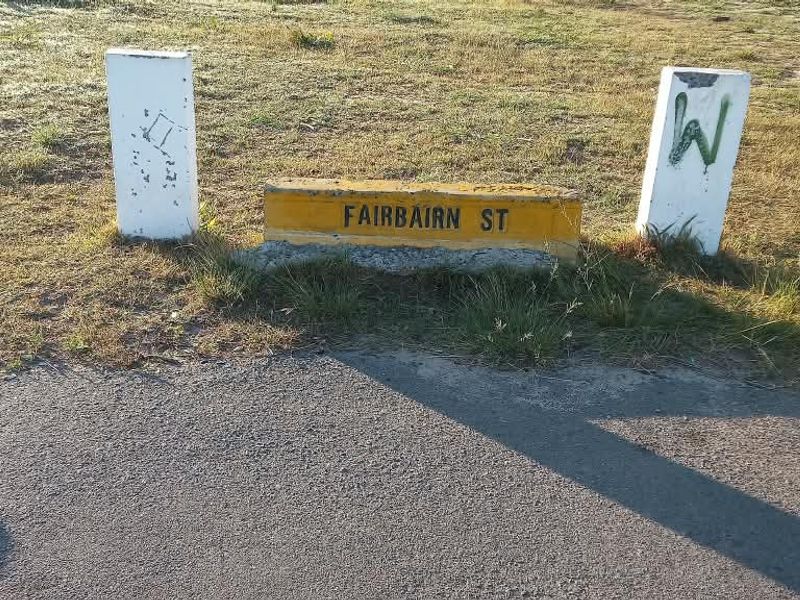 A street-level view of the property frontage featuring a Fairbairn Street sign and concrete bollards on a grass verge.