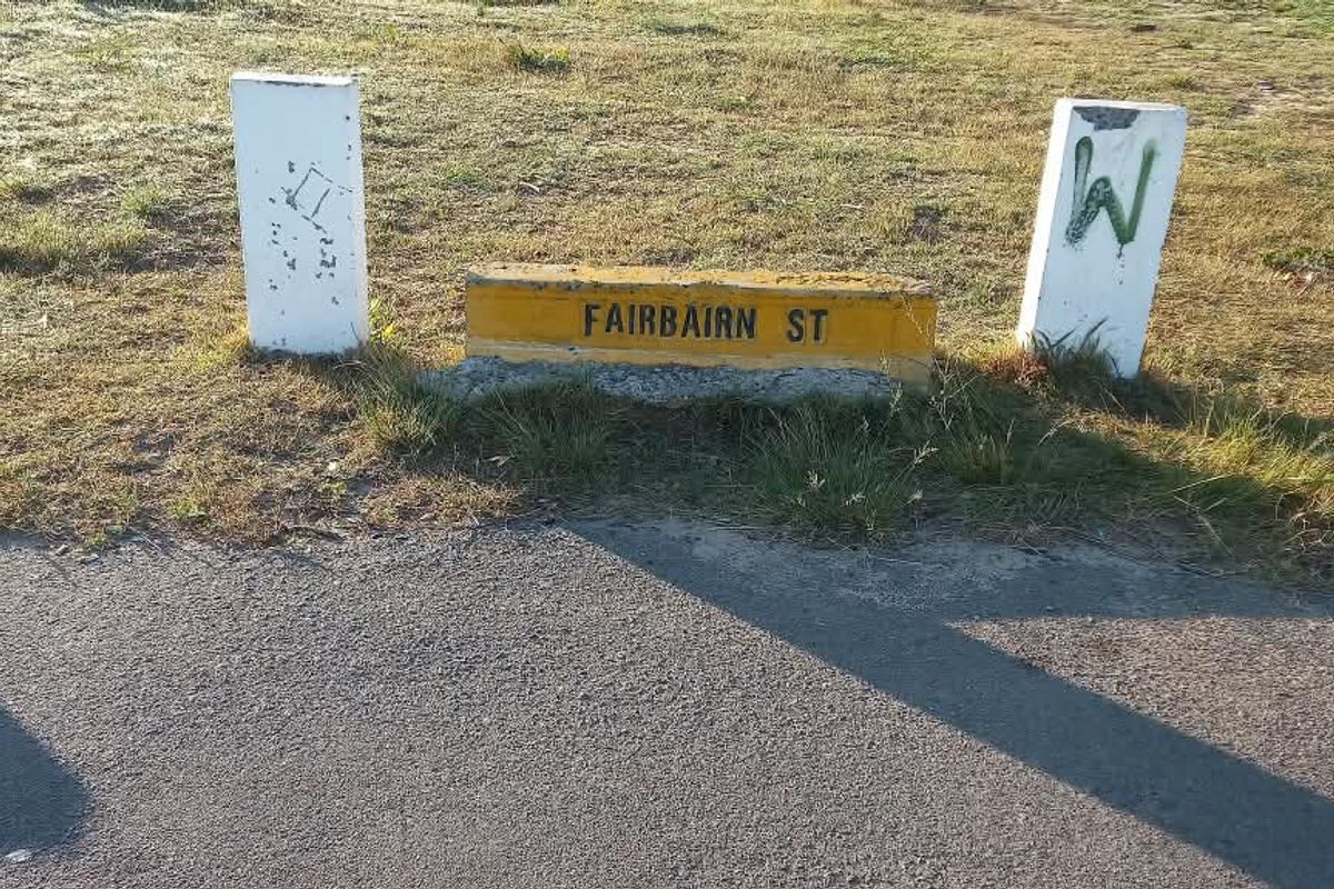 A street-level view of the property frontage featuring a Fairbairn Street sign and concrete bollards on a grass verge.