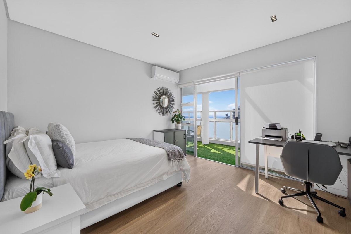 Modern bedroom featuring light timber flooring, recessed lighting, split-system air conditioning, and direct access to a private balcony with ocean views.