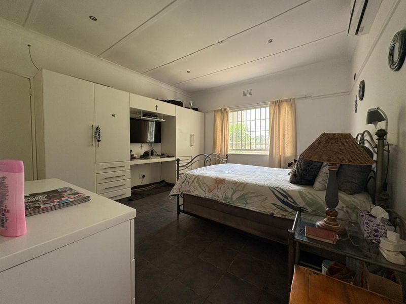 A functional bedroom featuring tiled flooring, built-in cabinetry with an integrated desk, and an air conditioning unit.