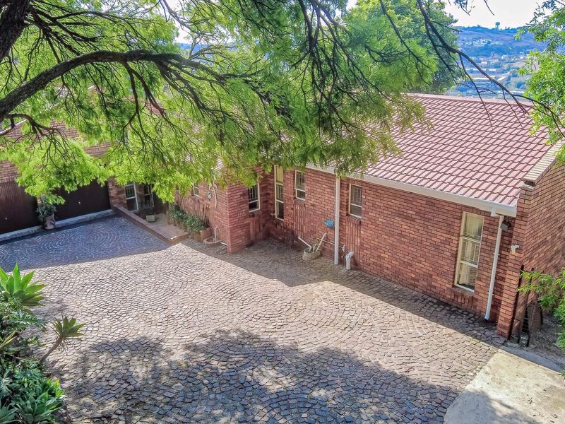 Elevated view of the front exterior featuring a classic brick facade, tiled roof, and a spacious cobblestone driveway leading to the garage.