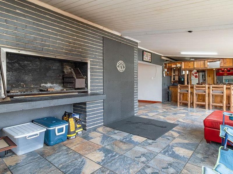 Covered patio area featuring a large built-in brick braai, tiled flooring, and a rustic built-in bar counter, ideal for outdoor entertaining.