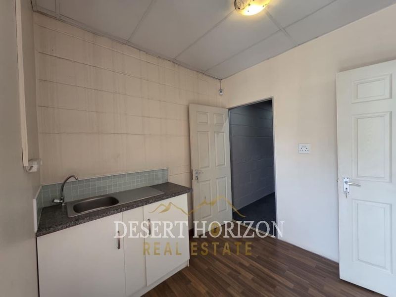 A compact kitchenette featuring a single sink, laminate countertop, base cabinetry, and tiled splashback, finished with a drop ceiling and laminate flooring.