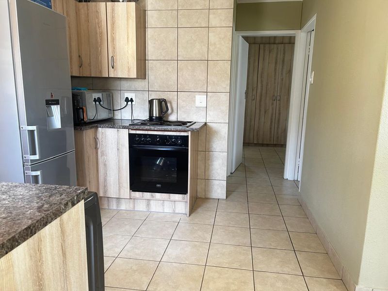 A functional kitchen featuring wood-look cabinetry, granite-style countertops, a built-in oven and hob, and neutral tiled flooring throughout.
