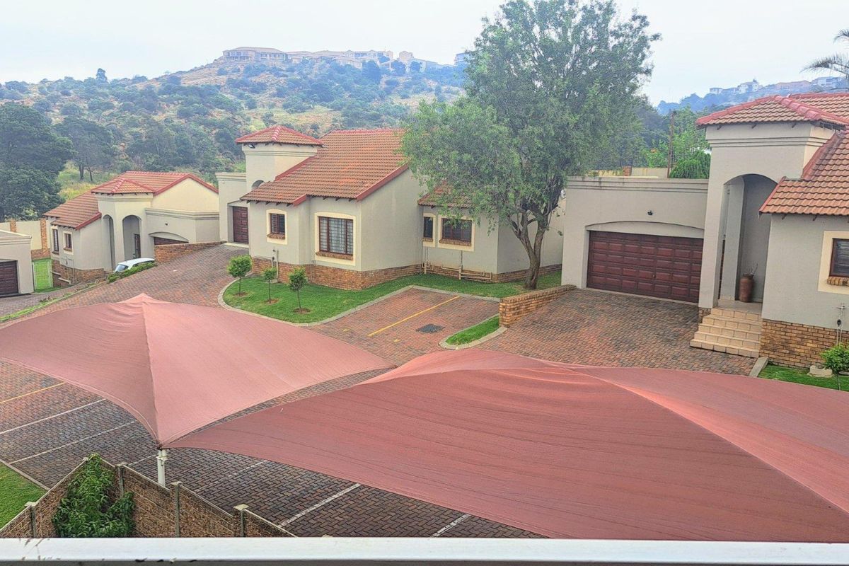 Elevated view of a townhouse complex featuring paved driveways, multiple garage units, and large shade sail structures over parking areas.