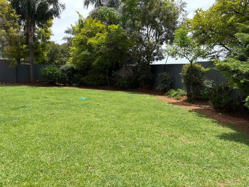 A well-maintained private garden featuring a lush green lawn, mature trees, and a secure perimeter wall with electric fencing.