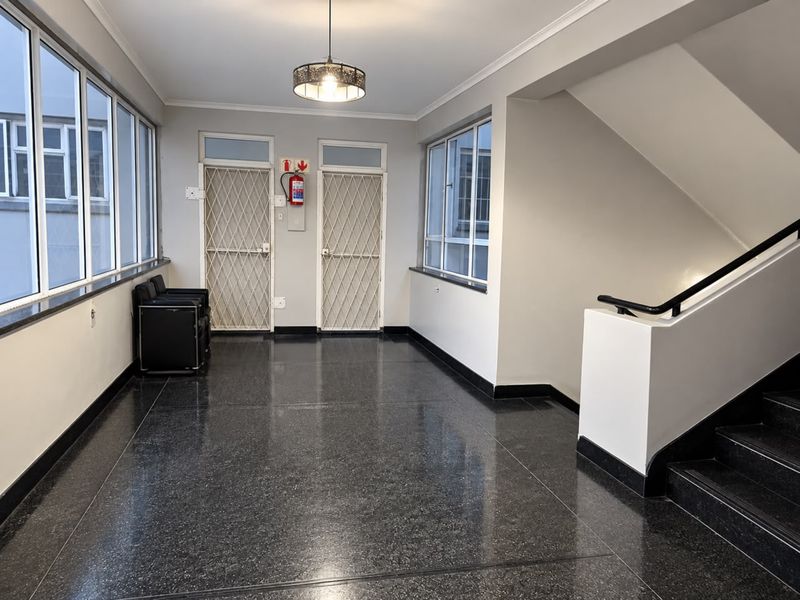 A clean and well-maintained apartment building hallway featuring terrazzo flooring, security gates, and a staircase with a handrail.