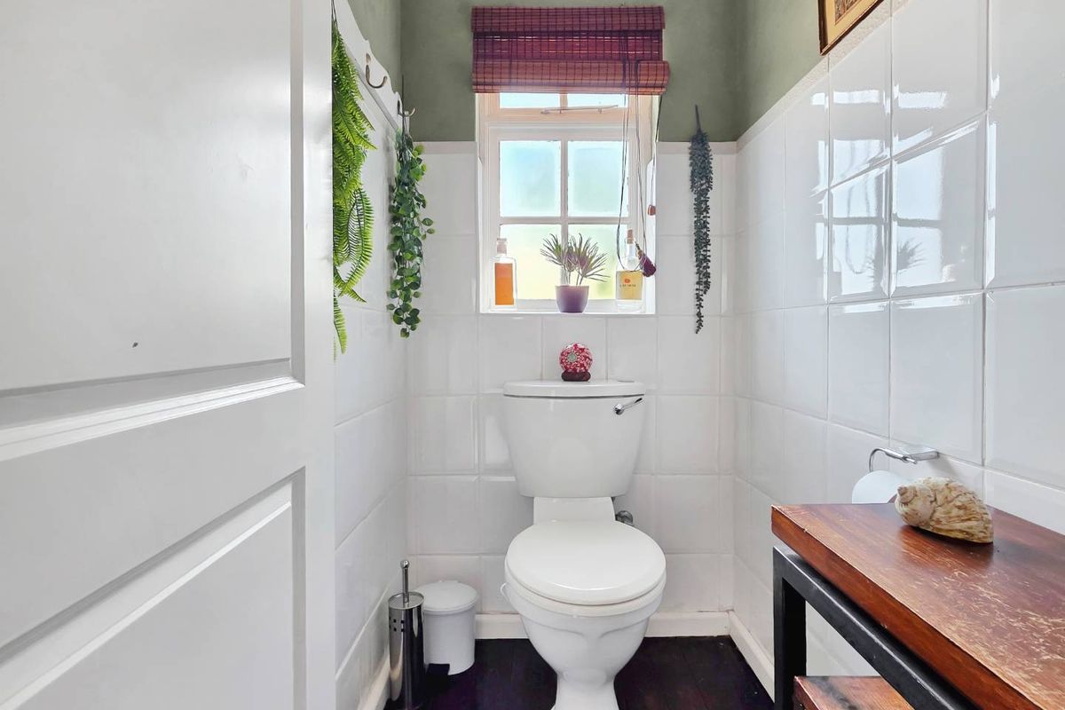 A compact bathroom featuring white wall tiles, a modern toilet, and a timber vanity unit with a window providing natural light.