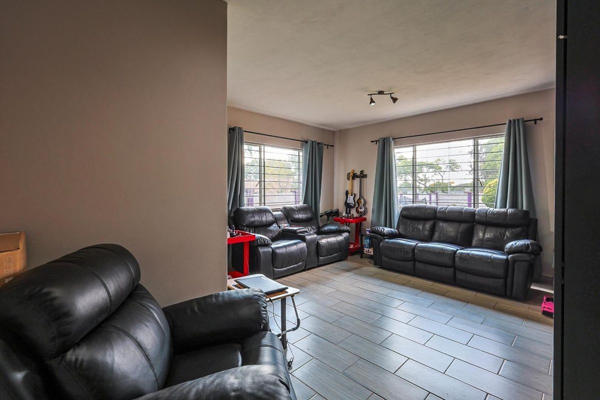 A spacious living room featuring large windows with security bars and modern tiled flooring.