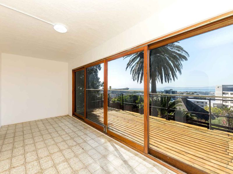 An empty balcony featuring wooden decking, metal railings, and large sliding glass doors that offer expansive views of the surrounding area.