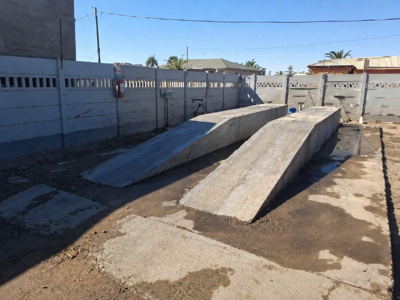 Outdoor utility area featuring dual concrete vehicle inspection ramps enclosed by a precast concrete boundary wall.