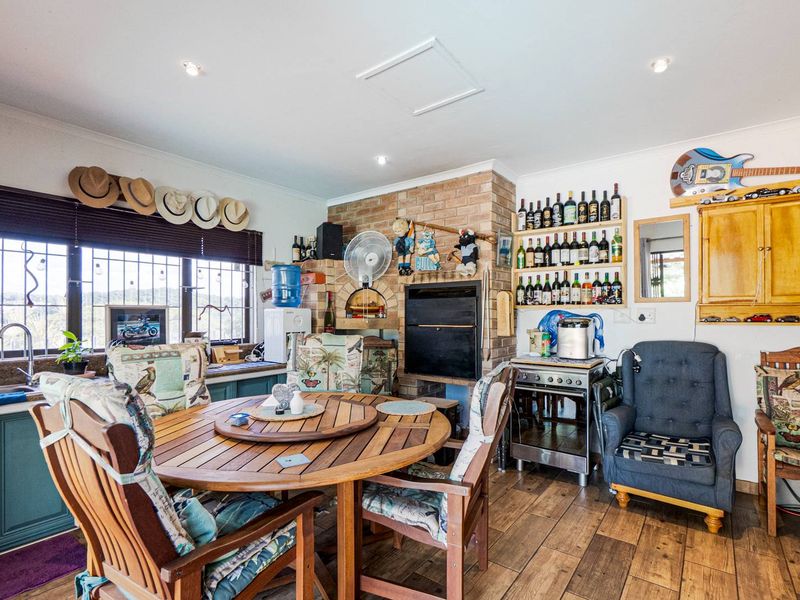 A rustic kitchen area featuring a built-in brick fireplace and braai, wooden cabinetry, and wood-look tile flooring with integrated lighting.