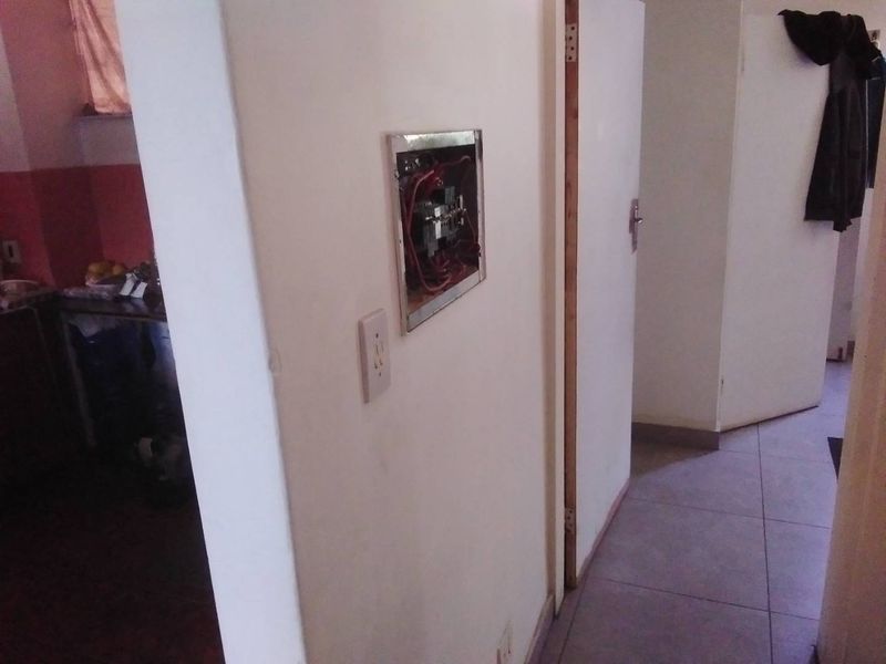 A hallway area featuring tiled flooring and an exposed electrical distribution board requiring a cover.