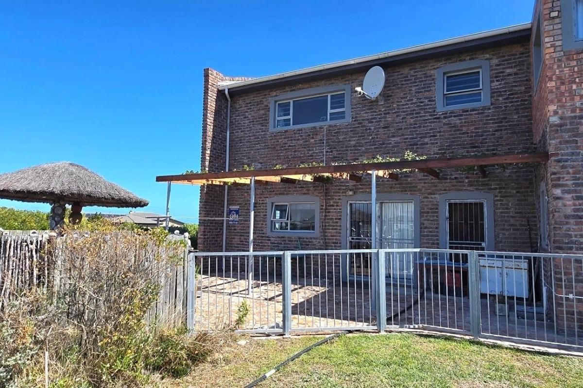 Rear view of a double-story brick house featuring a paved patio area, a timber pergola, and a fenced garden space.