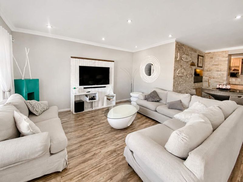 Spacious open-plan living area featuring modern laminate flooring, recessed lighting, and a textured stone feature wall, creating a bright and inviting atmosphere.