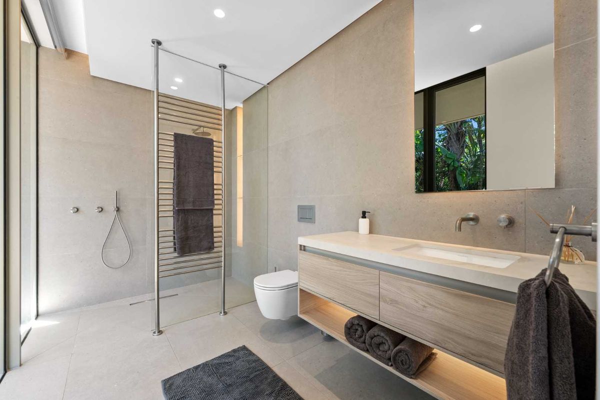 Modern bathroom featuring a floating vanity, wall-mounted toilet, walk-in shower with glass partition, and high-end stone tiling throughout.