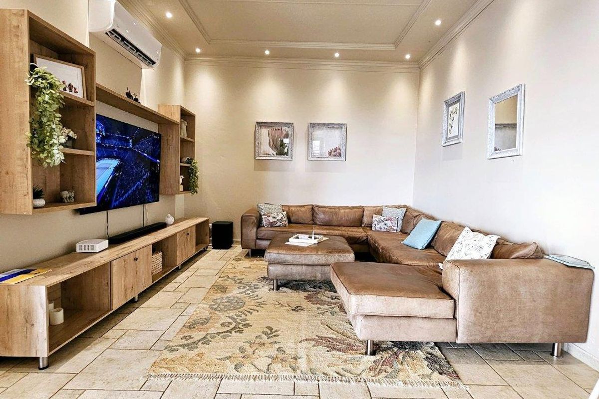 A well-maintained living room featuring tiled flooring, recessed ceiling lighting, crown molding, and custom built-in media cabinetry with an integrated air conditioning unit.