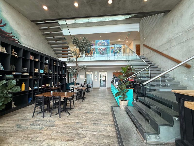 Modern open-plan office lobby featuring a striking floating staircase, glass balustrades, built-in shelving, and contemporary concrete wall finishes.