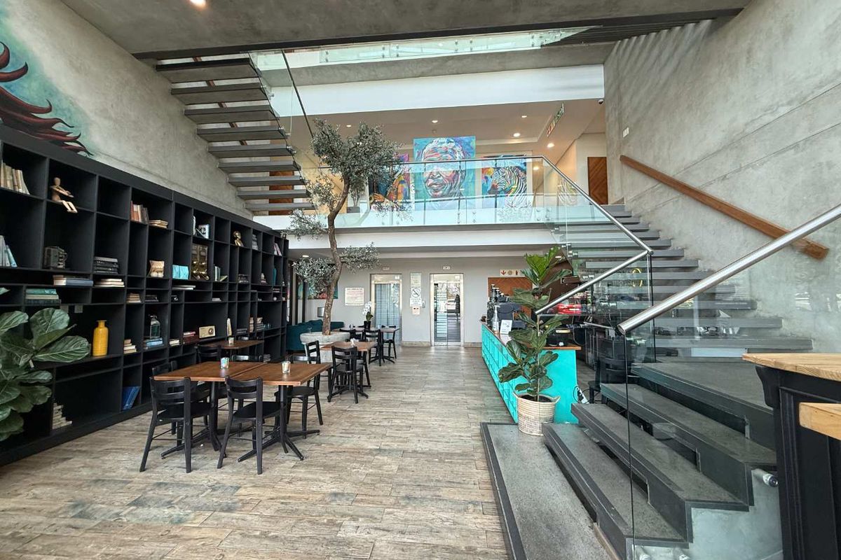 Modern open-plan office lobby featuring a striking floating staircase, glass balustrades, built-in shelving, and contemporary concrete wall finishes.