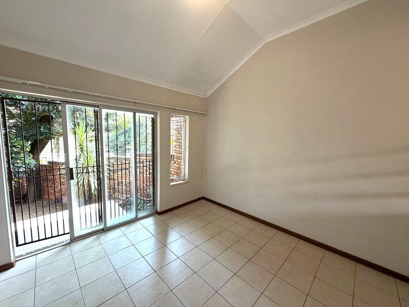 An empty living room featuring tiled flooring, a vaulted ceiling, and a sliding glass door with security bars leading to the exterior.