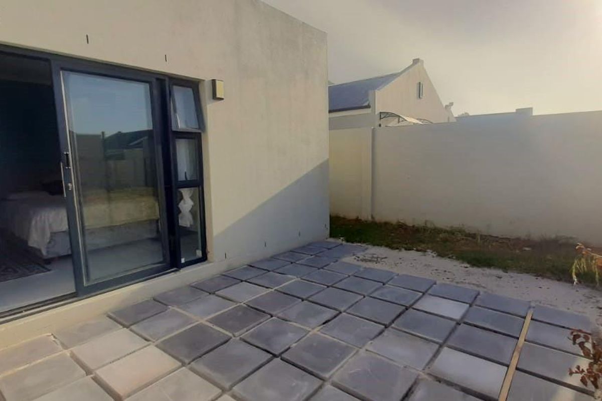 A rear patio area featuring paved flooring and sliding glass doors providing access to the interior living space, enclosed by a perimeter wall.