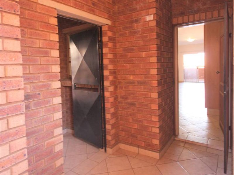 An entrance foyer featuring exposed brick walls and ceramic floor tiles, providing access to interior living spaces through a security gate.