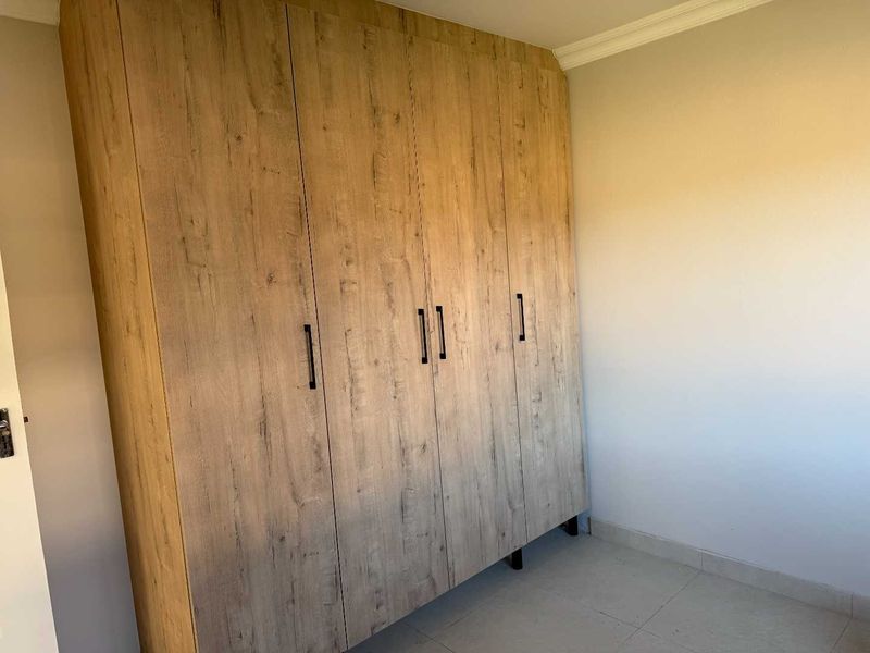 A clean, empty bedroom featuring modern wood-look built-in wardrobes and neutral tiled flooring, offering a versatile space ready for personalization.