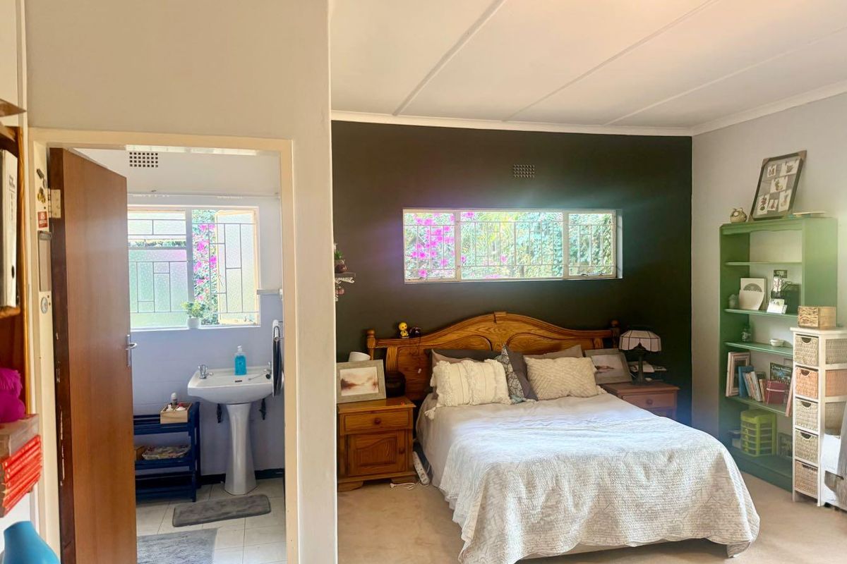 A bedroom featuring a dark accent wall, carpeted flooring, and an adjoining en-suite bathroom with a pedestal basin and tiled floors.