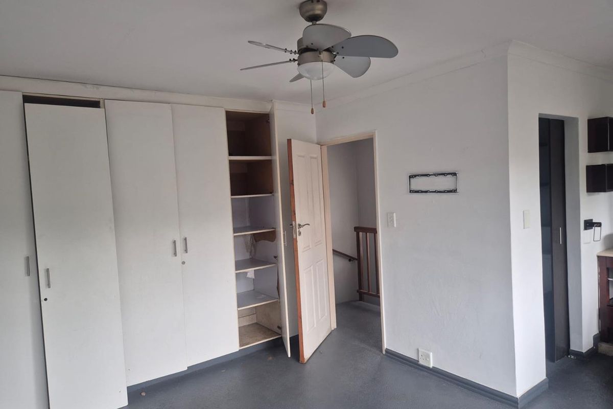 A bedroom featuring built-in cupboards with open shelving, a ceiling fan, and direct access to a staircase area.